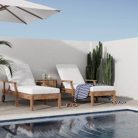 Zwei Liegen mit weißen Kissen neben einem Pool, umgeben von Pflanzen und Sonnenschirm.