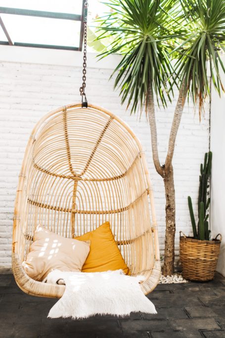 Hängesessel aus Rattan mit Kissen und Pflanzen im Hintergrund.
