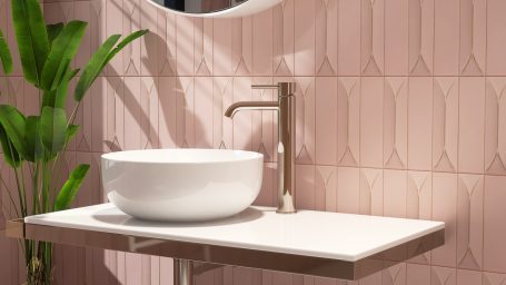 Schlichte Waschbeckenmontage mit runder Schüssel und modernen Armaturen vor rosa Fliesen.