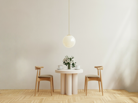 Ein runder Tisch mit Blumenarrangement und zwei Holzhockern in einem hellen Raum.