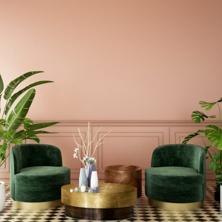 Zwei grüne Sessel und runder Tisch vor einer rosa Wand mit Pflanzen im Hintergrund.